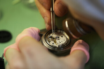 Macro image of unrecognizable watchmaker using tweezers while assembling mechanical watch