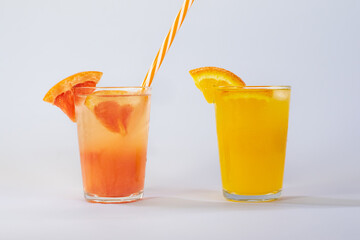 Photo of a glass of grapefruit juice with a red and white straw and a glass of orange juice on a white background