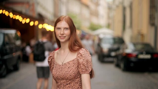 Beautiful Young Woman with long red hair walking on the street look at camera. Female model with natural beauty and lovely freckles on her Face