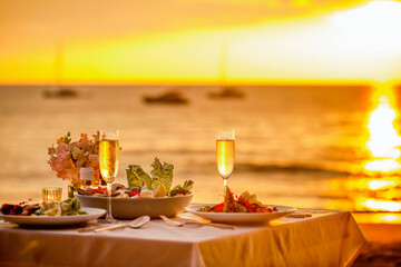 Romantic sunset dinner on the beach. Table honeymoon set for two with luxurious food, glasses of...