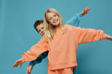 two cute children of school age in multi-colored sweaters stand on a blue background, a boy and a girl stand with their hands apart, depicting airplanes. The theme of friendship between children