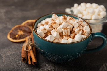 Cup of tasty cocoa drink and marshmallows in blue cup.Spices and marshmallows for winter drinks on black texture table.Winter hot drink.Hot chocolate with marshmallow and spices.Copy space.