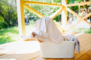 Funny funny child toddler in basket with clean linen on summer veranda of house, summer vacation...