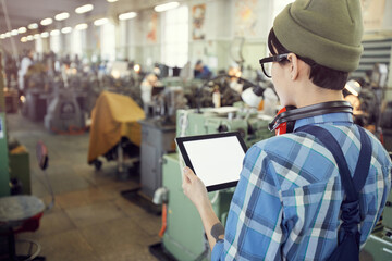 Rear view of hipster factory supervisor using digital tablet while controlling production processes at factory
