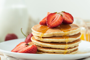 American pancakes decorated with strawberries, drizzled with honey and sprinkled with powdered sugar in a white plate. Healthy and tasty breakfast
