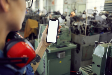 Factory worker with tattoo on arm standing in industrial shop and using smartphone while photographing manual machines