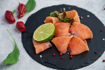 Fresh smoked salmon slices with peppers, greens and lime on concrete background
