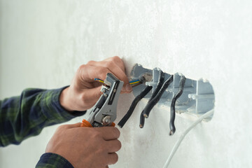 Electrician mounts a new socket on a white wall. Renovation process in a new apartment