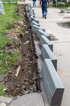 New curbs stand at the edge of the sidewalk. Preparing to repair road