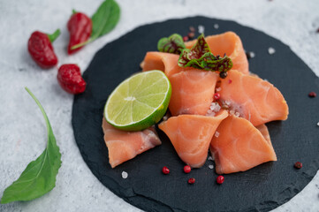 Fresh smoked salmon slices with peppers, greens and lime on concrete background