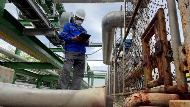 Production engineers inspect industrial equipment at pipeline at factory. Referent holding a tablet with a design sheet. Concept of industry and technology
