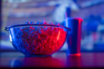 A cozy evening at home, in front of the TV. A large glass bowl with popcorn, soda drink in a glass on the background of the TV screen. Neon lighting. Favorite series, sports and music programs.