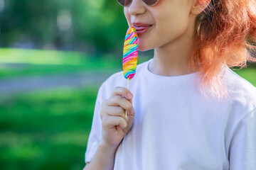 A teenage girl in a white casual T-shirt with a multi-colored lollipop in her hand. Front view of t-shirt mockup for design print. Summer vacation in the park. 