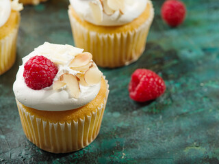 Cupcakes with white cream, raspberries and almonds on a dark green background. Children and youth culture, fast food, light summer dessert, birthday, holiday treat.