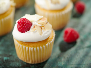 Close-up. Festive treat - berry muffins with light white cream, raspberries and almonds. Isolated on a green background. Food background. Birthday invitation, banner.