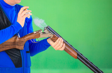 Clay pigeon shooting. An athlete shoots a gun at moving targets isolated on a green background,...