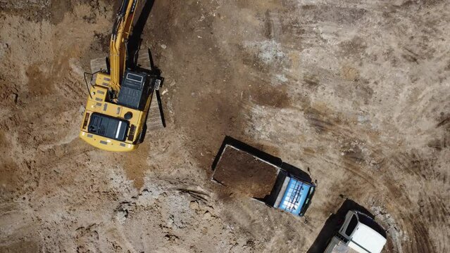Excavator scoop loads a soil in dump truck on preparing place to construction site for prepare build building structure, Aerial view