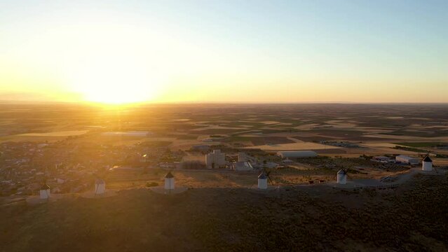 Aerial view of Windmill of Consegro. Famouse travel destination in Toledo. Sun in front of the camera at sunrise. Beautiful Warm colours. Drone pan right and sun moving from one windmill to another