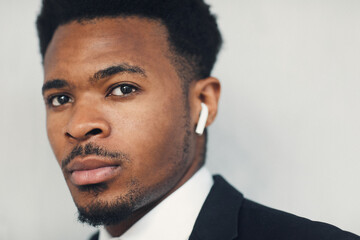 Close-up of serious young Afro-American businessman using Bluetooth earbuds for communication on...