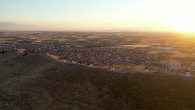 Aerial view of Windmill of Consuegra. Underexposed video at sunrise.  Sun in right corner of the camera at sunrise. Beautiful Warm colours. Drone dolly forward to windmill 
