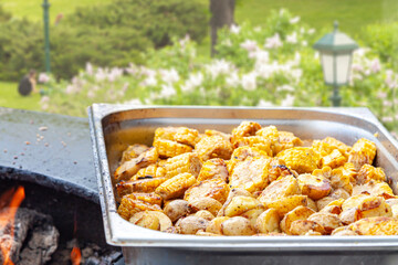 Grilled potato slices roasting on an open fire pit with a hand holding tongs, outdoor cooking concept