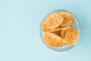 Potato chips in glass bowl on blue background. Fast food.