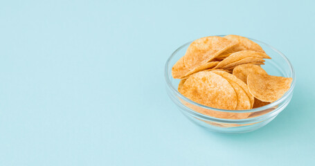 Potato chips in glass bowl on blue background. Fast food.