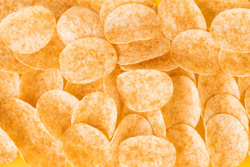 Background and texture of a heap of rotating potato chips on yellow background. View from above.