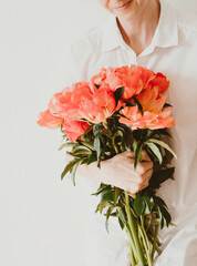 Young woman in white clothes holds large bouquet of coral-colored peonies.