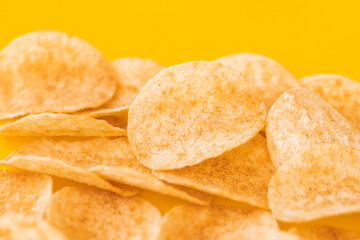 Background and texture of a heap of rotating potato chips on yellow background. View from above.