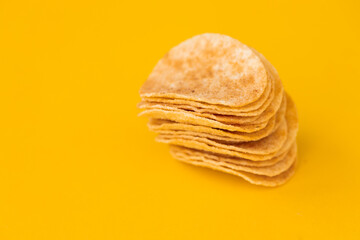 Background and texture of a heap of rotating potato chips on yellow background. View from above.