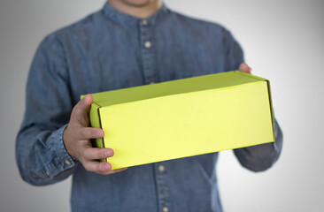 A man holds a yellow box. On a gray background