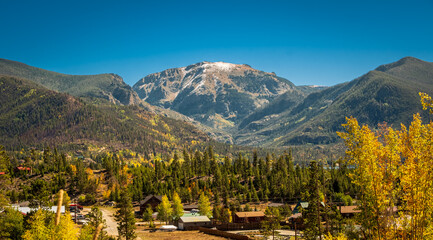 Fototapeta na wymiar Panoramic view of beautiful mountain range powdered with snow in Rocky Mountain, Colorado, and small town at foothills; blue sky in background