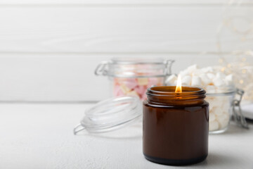 Cozy burning candle in brown glass jar on white texture wood.winter home decor.Soy ecological...