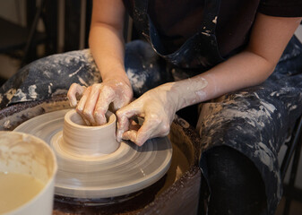 A woman works on a potter's wheel. Hands form a cup of wet clay on a potter's wheel. Artistic...