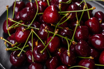 Fresh sweet cherries plate with leaves in water drops on stone background, top view