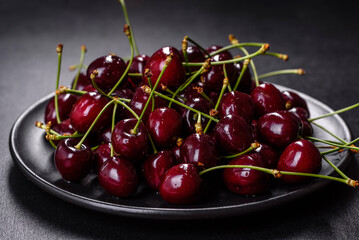 Fresh sweet cherries plate with leaves in water drops on stone background, top view