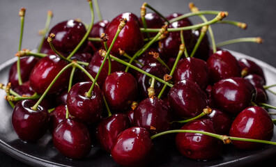 Fresh sweet cherries plate with leaves in water drops on stone background, top view