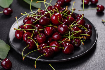 Fresh sweet cherries plate with leaves in water drops on stone background, top view