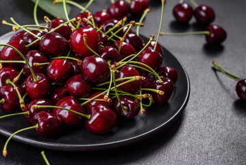 Fresh sweet cherries plate with leaves in water drops on stone background, top view