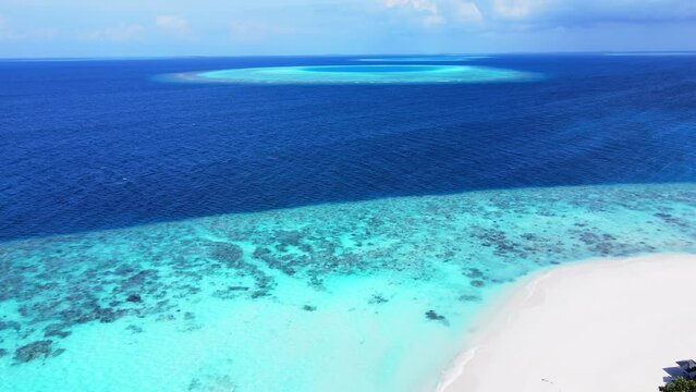 Tropical atoll island in Maldives with coral reef and turquoise sea water. Touristic vacation holidays travel destination. Scenic seascape. Drone aerial video footage.
