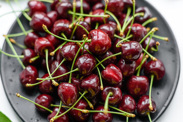 Fresh sweet cherries plate with leaves in water drops on stone background, top view