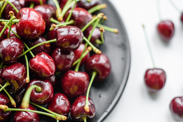 Fresh sweet cherries plate with leaves in water drops on stone background, top view
