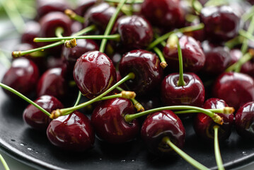 Fresh sweet cherries plate with leaves in water drops on stone background, top view