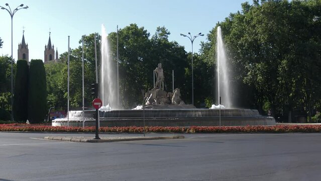 4K video of the Neptune fountain with large jets of water, cars and buses going through the roundabout it is located on in Madrid, Spain