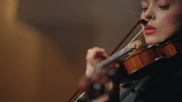 young woman fiddler is playing violin in philharmonic hall, closeup portrait of female violinist