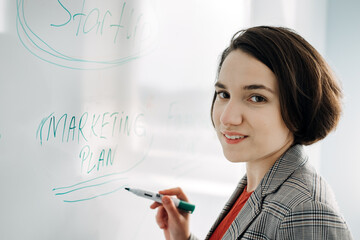 Startup Business Plan. Young businesswoman manager, team leader, Investor writing on the board business plan