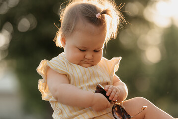 A close portrait of a pretty female toddler in yellow clothes who is enthusiastically playing with...