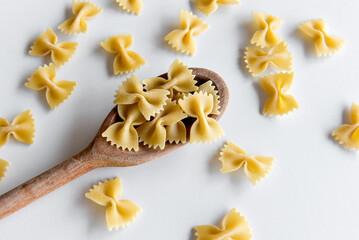 raw tie pasta on wooden spoon and white background (farfalle pasta).