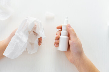 Child hands hold bottle nose spray and paper tissue on white background. Runny nose treatment